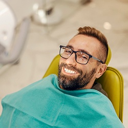Man with glasses smiling while sitting in treatment chair
