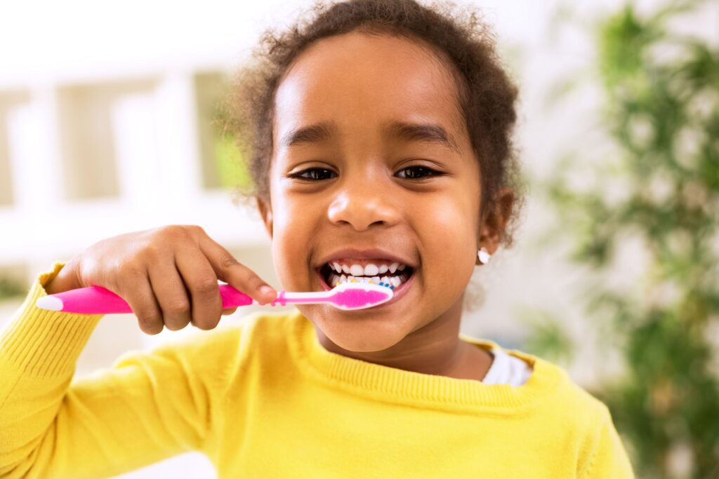 Little girl in yellow sweater brushing her teeth